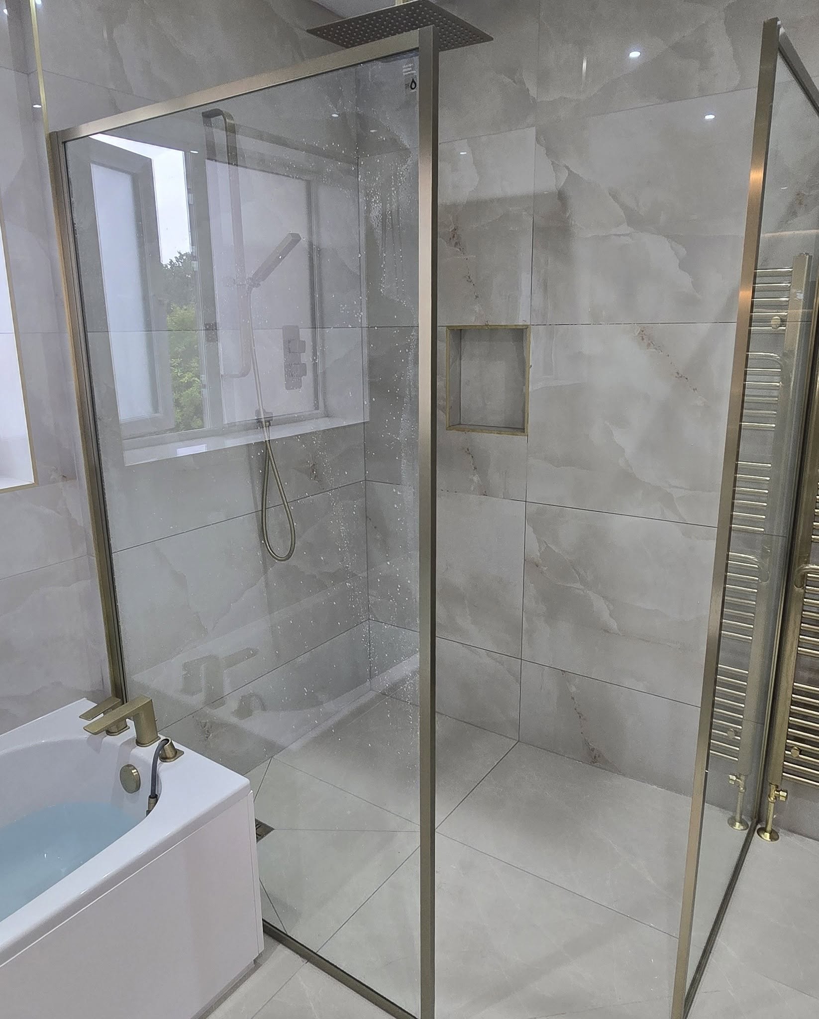 Walk-in shower with a brushed-brass frame, rainfall head and tiled niche