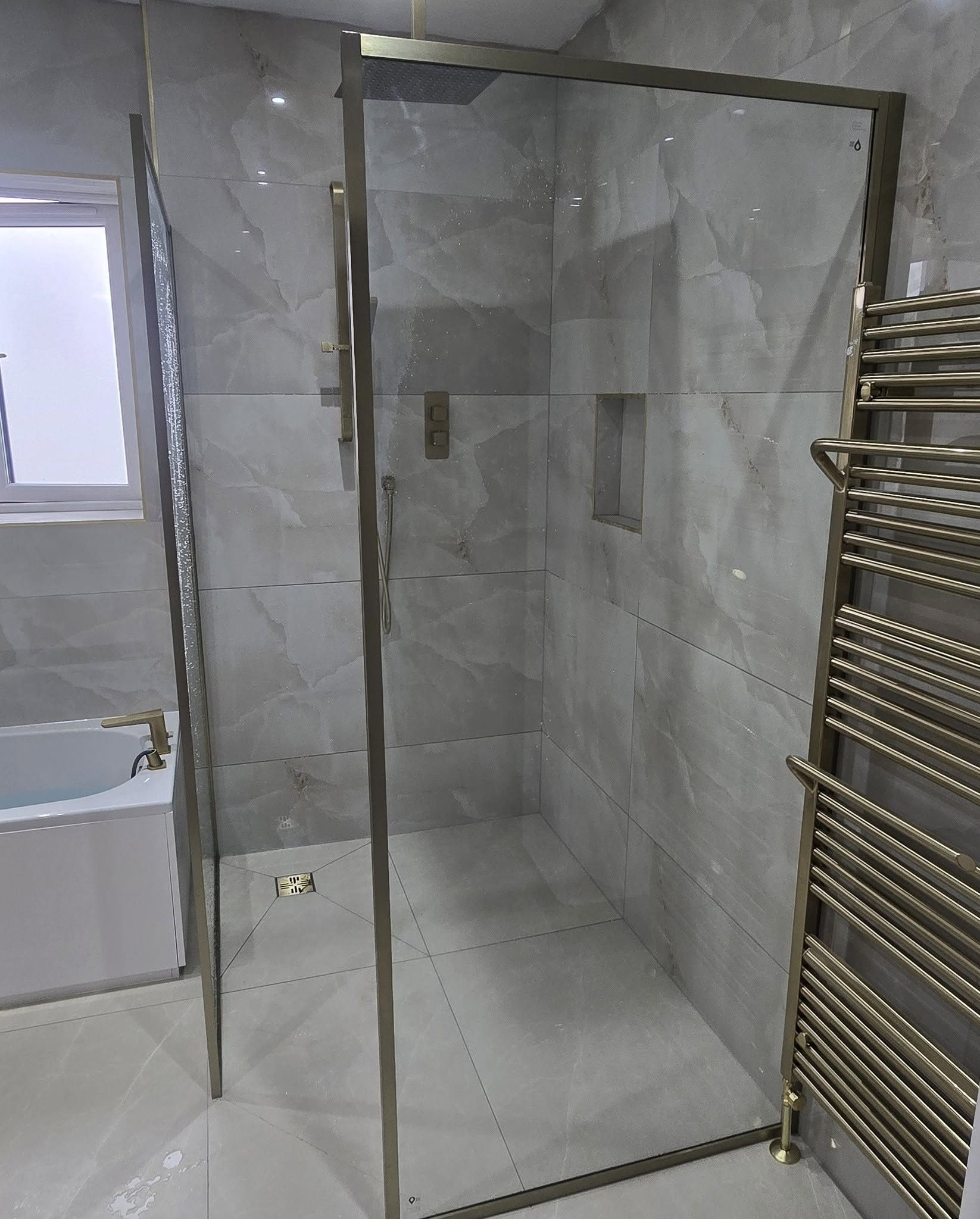 Walk-in shower enclosure with a brushed-brass frame beside a brass towel rail