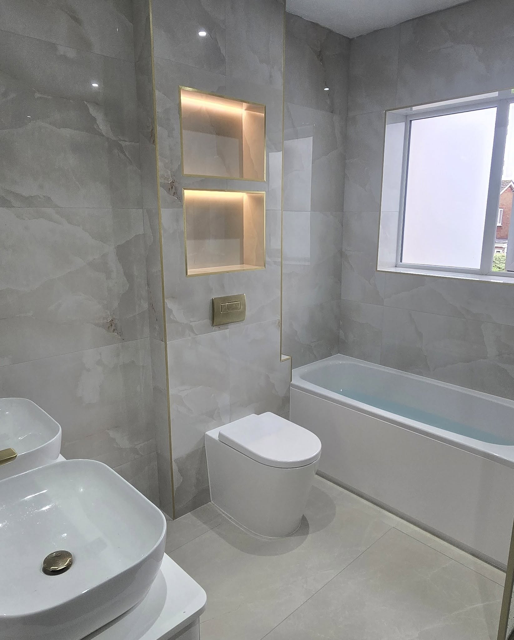 Lit shelf niches above a wall-hung toilet, with the bath beyond