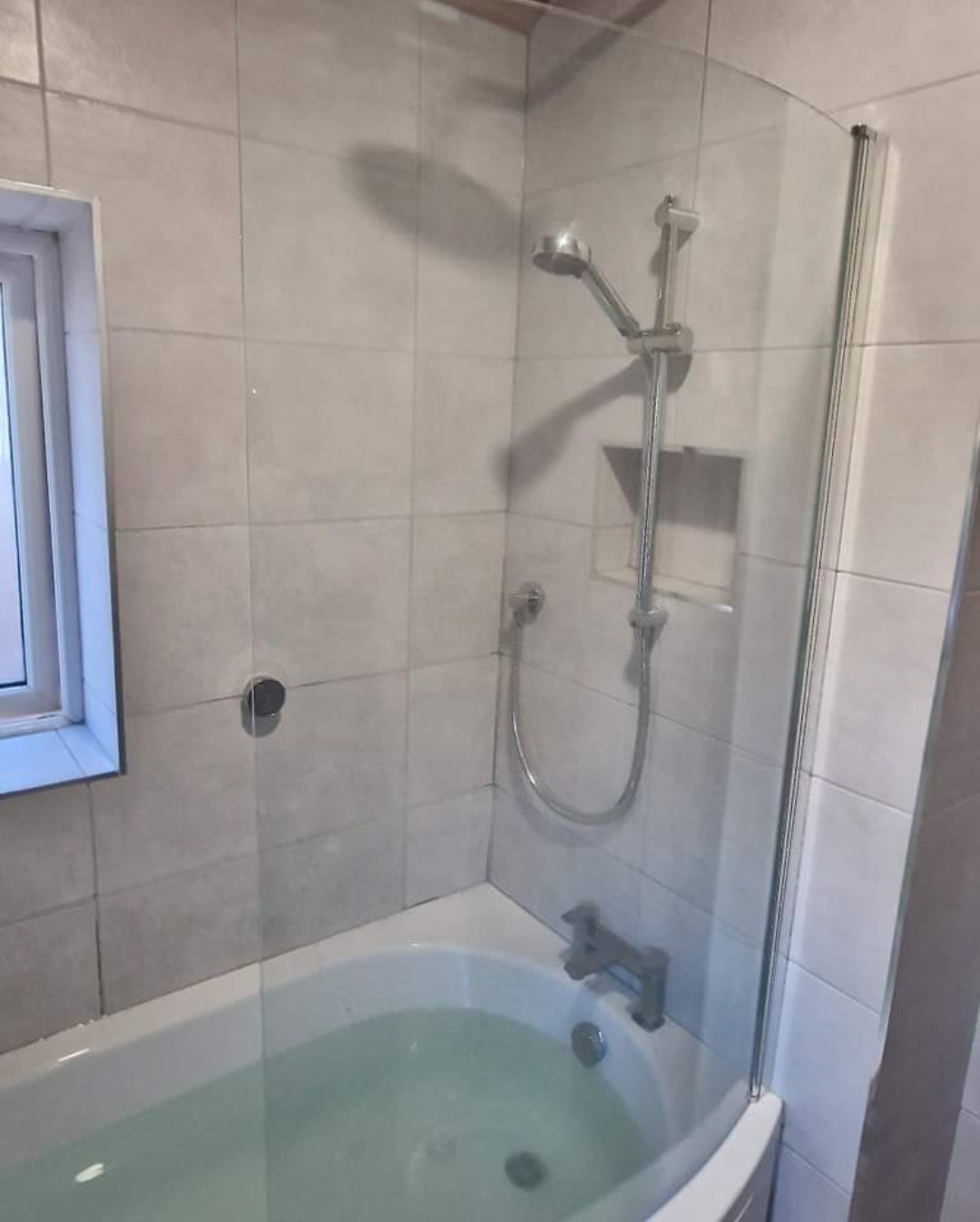 Bath with a glass shower screen and slide-rail shower in a tiled bathroom