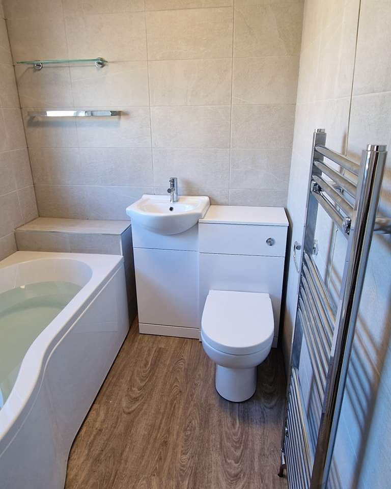 Bathroom with a shaped bath, white vanity unit and chrome towel rail